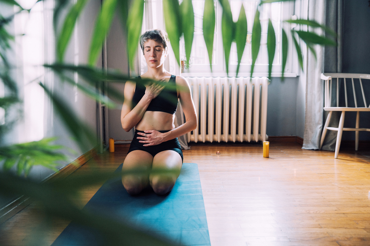 Young woman practices deep breathing by kneeling and placing hand on her chest and hand on her stomach
