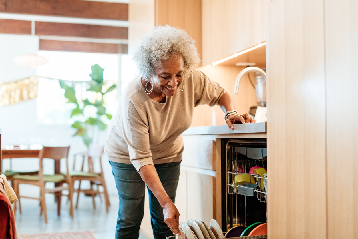 Smiling senior woman putting plates in dishwasher. This is an example of how movement can be added into a person's daily routine.